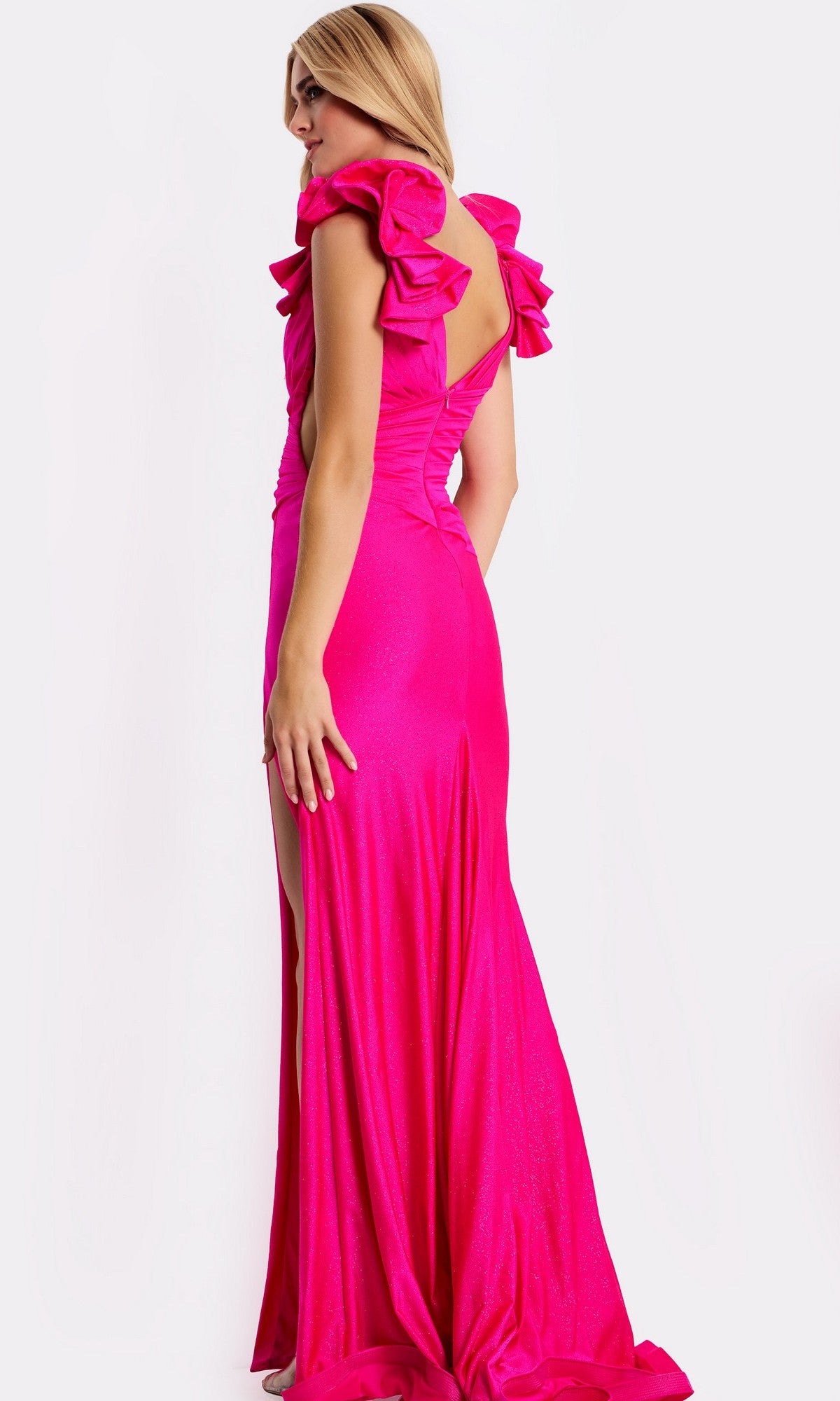A woman models the Jovani 46496, a bright pink long prom dress featuring ruffle shoulder straps and a high-leg slit, as she stands looking over her shoulder.